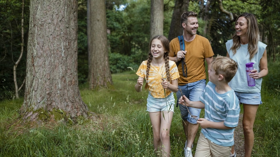 An adult couple and their young son and daughter having a great time walking on the grass through woodlands